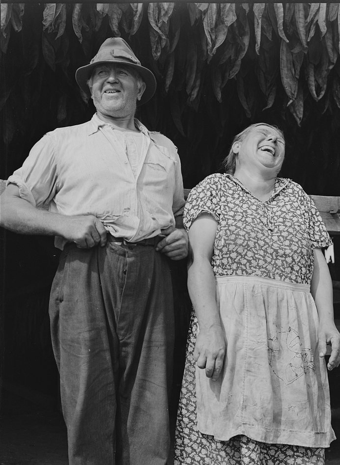 A Polish-American farming couple laughing in front of a tobacco barn